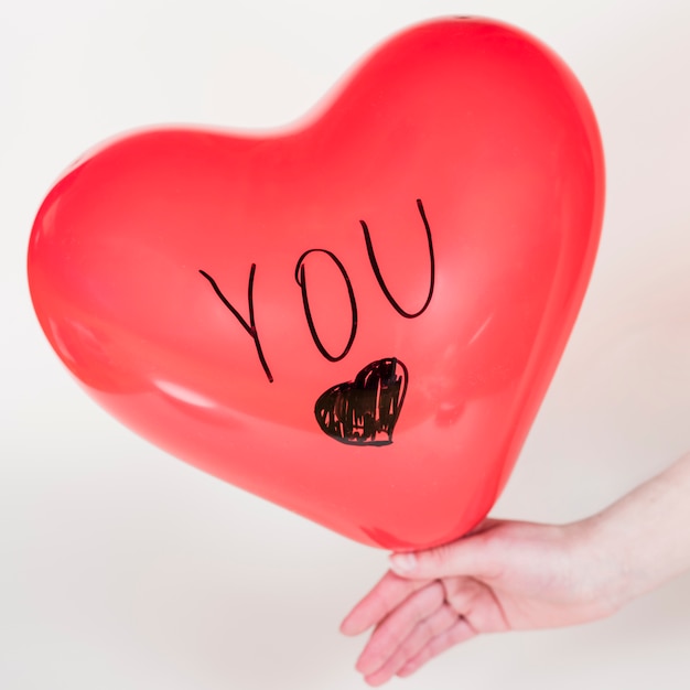 Person holding heart balloon with You inscription 