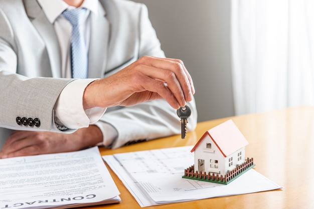 Person holding house keys and toy model house on desk