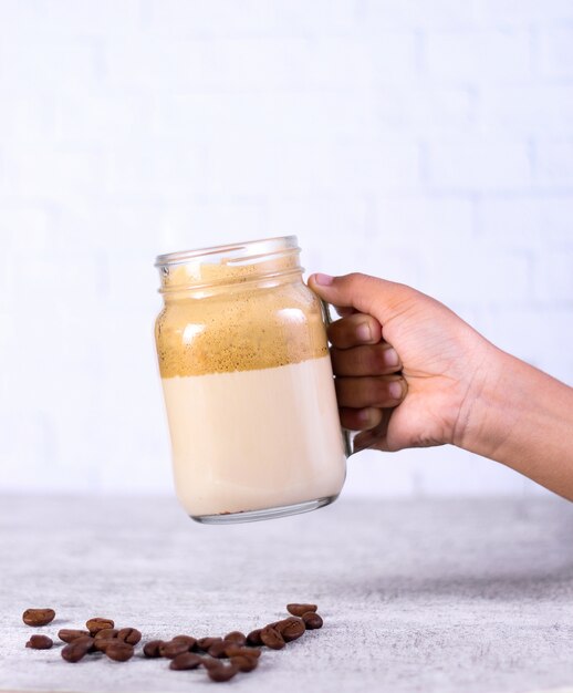 Person holding a jar of caramel smoothie over coffee beans on white