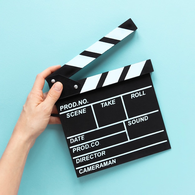 Person holding movie clapper on blue background