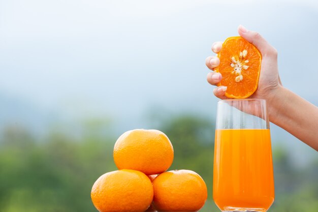 Person holding an orange fruit in her hand and squeezing it in a jar