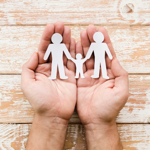 Person holding paper family in hands on wooden background