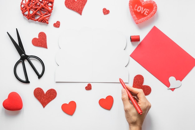 Person holding pen above table with hearts 