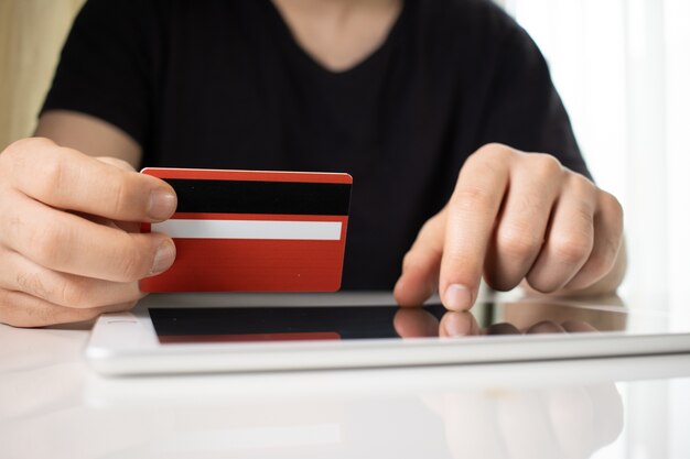 Person holding a red credit card over a tablet on a white surface