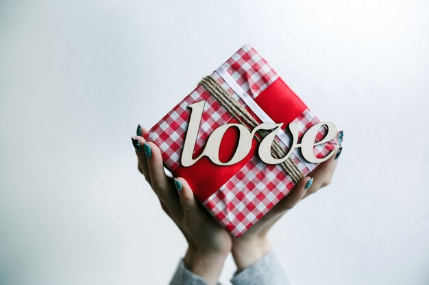 Person holding red gift with word "love" in a white background