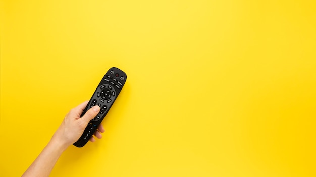 Person holding remote on yellow background with copy space