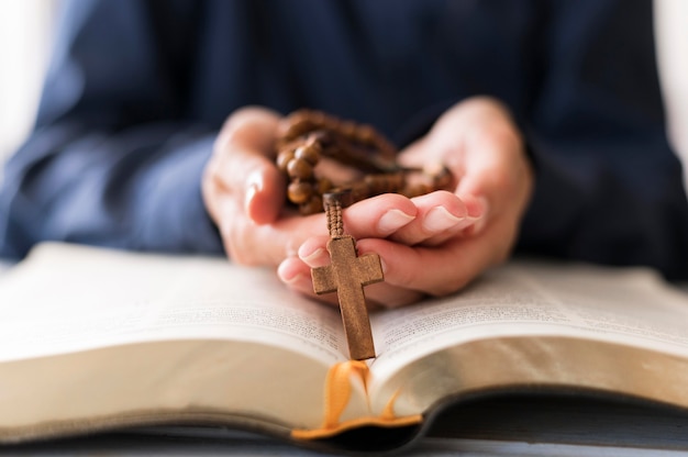 Person holding rosary with cross on open holy book