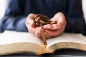 Free photo person holding rosary with cross on open holy book