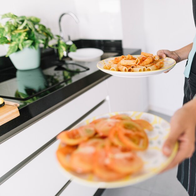 Человек, содержащий ломтики томатов и вкусные макароны на тарелке