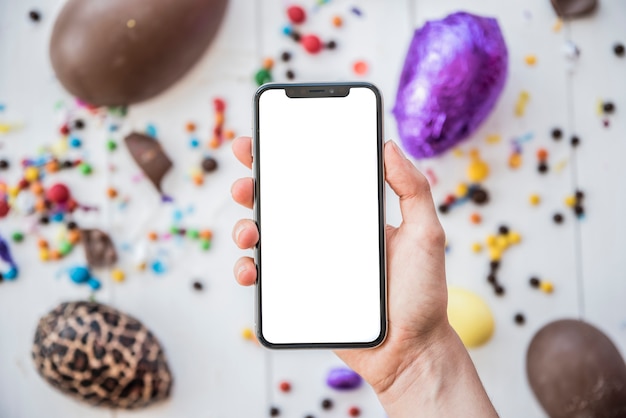 Person holding smartphone with blank screen above Easter eggs 