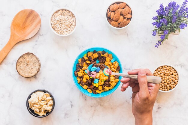 Person holding spoon with cereal above bowl