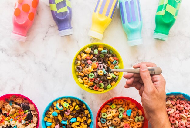 Person holding spoon with cereal above bowl 