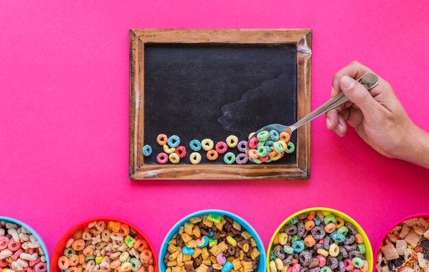 Person holding spoon with cereal above chalkboard 