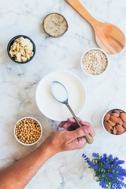 Person holding spoon with milk above bowl on table 