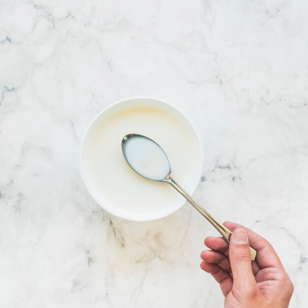 Person holding spoon with milk above bowl 