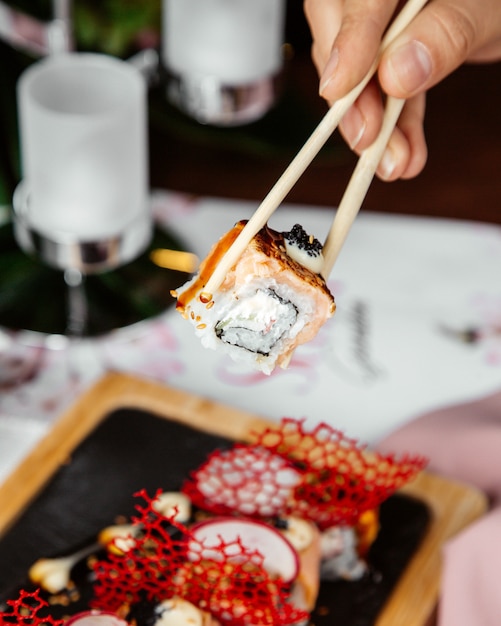 A person holding sushi with sticks