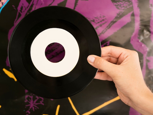 Person holding vinyl record disk near colorful wall