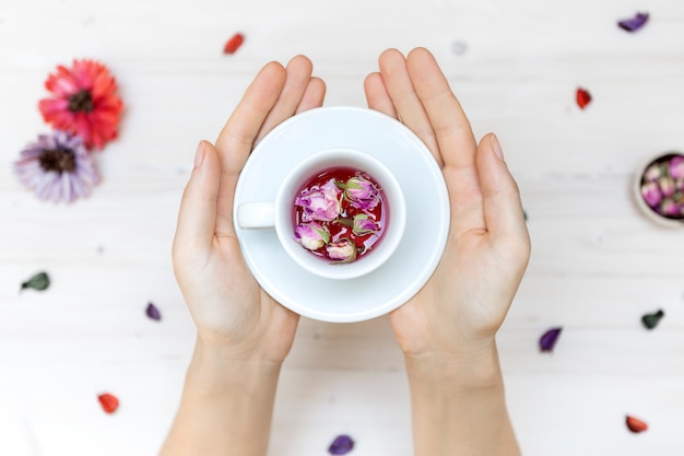 Foto gratuita persona in possesso di una tazza da tè bianco con petali di rosa