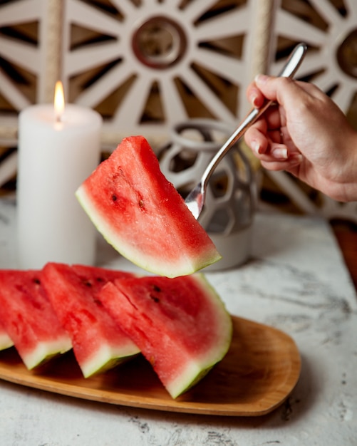 A person holding with fork a slice of watermelon