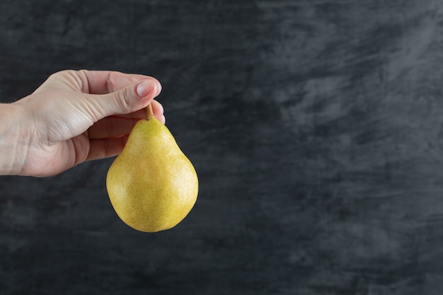 A person holding a yellow pear from the stem