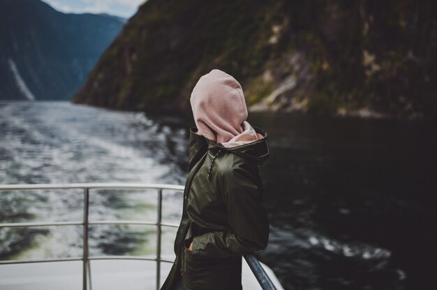 Person in a hoodie standing on the ship during the cruise in Milford Sound in New Zealand