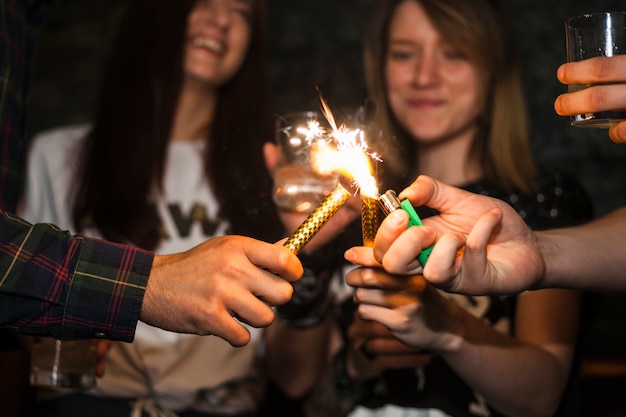 A person lighting sparkle candle with cigarette lighter with friends