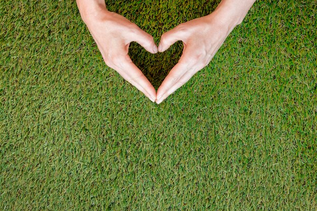 Person making a heart with his hands on grass with copy space