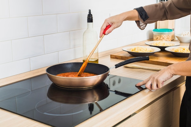 Person mixing sauce in pan on stove