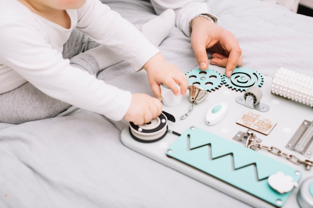 Free photo person near little baby with toy sitting on bed