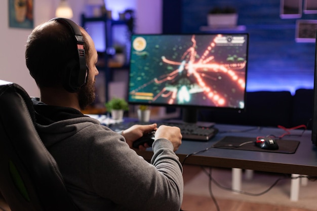 컴퓨터에서 컨트롤러로 비디오 게임을 하는 사람. 플레이어는 조이스틱을 사용하고 헤드폰을 착용하여 모니터에서 온라인 게임을 합니다. 재미를 위해 게임 장비를 사용하는 현대인.