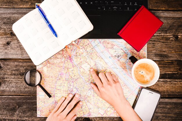 Person pointing at destination on map with cup of coffee and diary on table