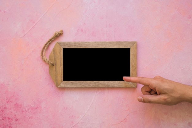 A person pointing finger to small tag slate on pink painted background