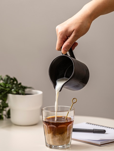 Person pouring cream in coffee glass