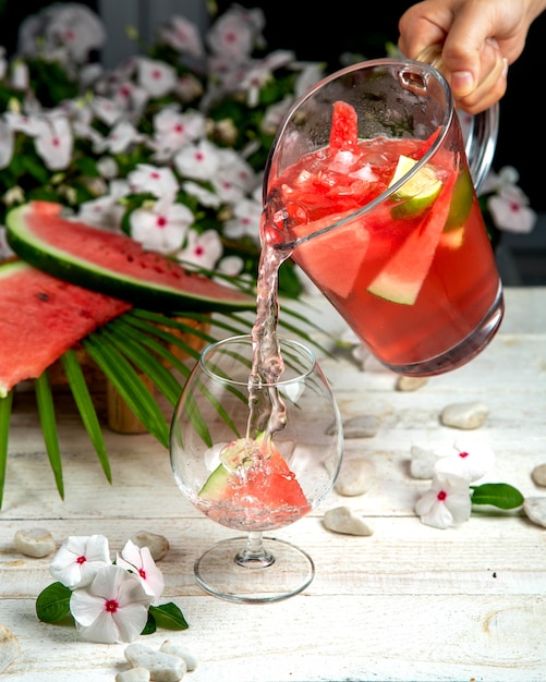 A person pouring homemade watermelon ice tea into a glass