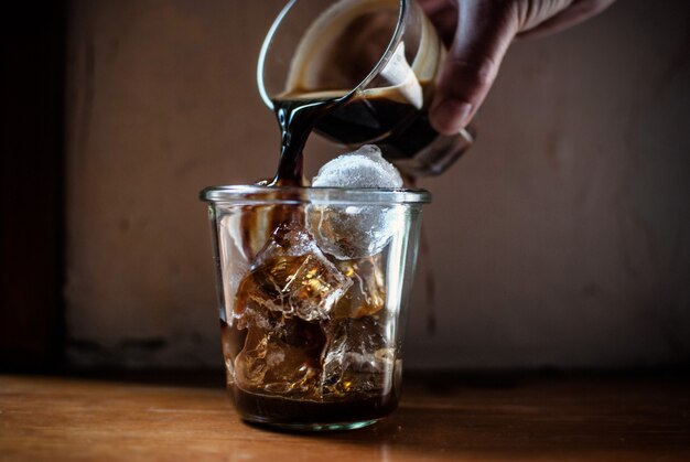 Person pouring hot coffee in a glass with ice