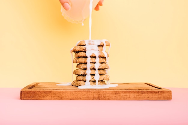 Person pouring milk from glass on cookies stack on board