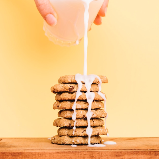 Person pouring milk from glass on cookies stack