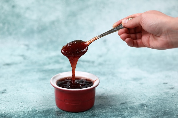 Foto gratuita una persona che versa marmellata di fragole in una tazza rossa.