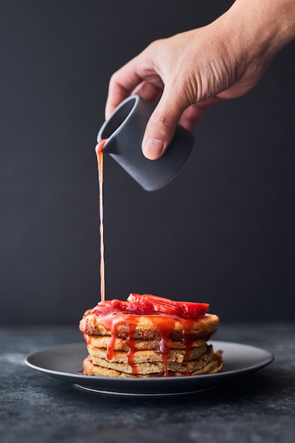 パンケーキのスタックにイチゴソースを注ぐ人