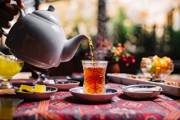 Free photo person pouring tea in armudy jam lemon side view