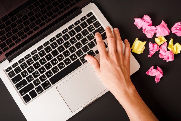 A person pressing button on laptop with pink and yellow crumpled papers on black background