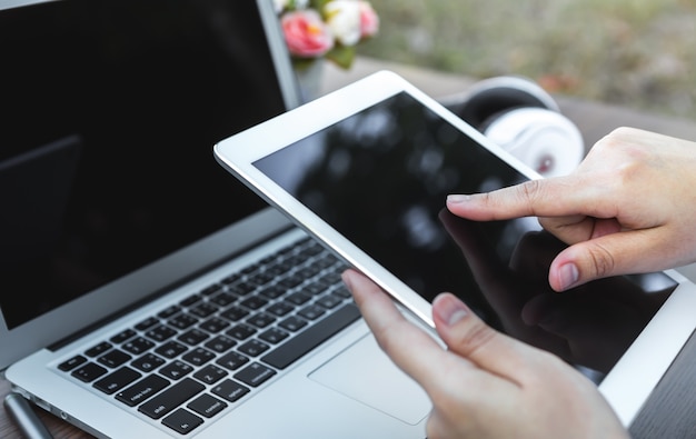 Person pressing the screen of a tablet with a laptop background