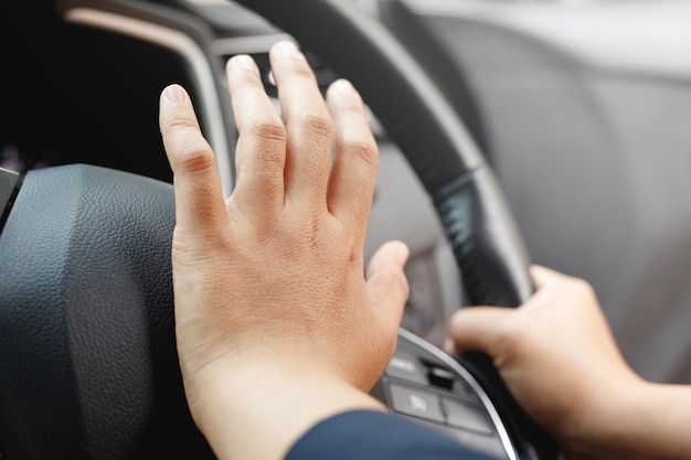 Человек толкает гудок во время вождения автомобиля пресса рулевого колеса, подавая звуковой сигнал, чтобы предупредить других людей в дорожной обстановке.