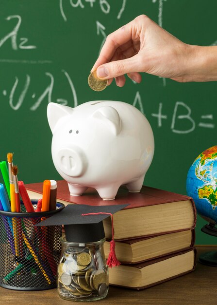 Person putting coins in piggy bank with books and academic cap