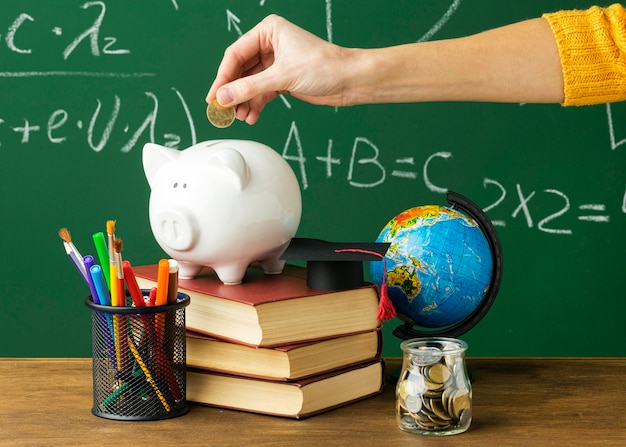 Free photo person putting coins in piggy bank with books and pencils