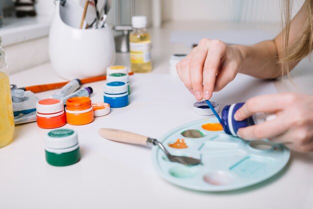 Person putting gouache on palette at white table