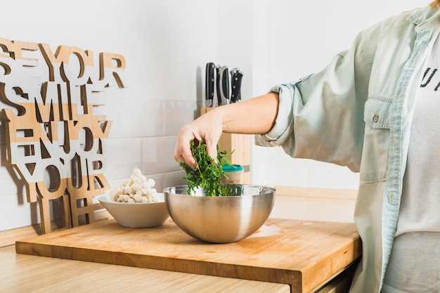 Foto gratuita la persona che mette la lattuga lascia in ciotola in cucina