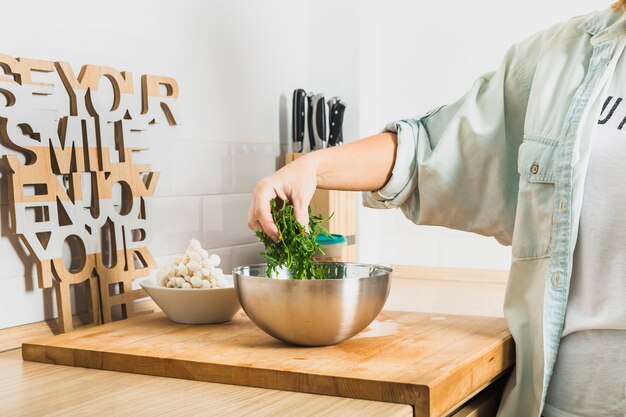 person putting lettuce leaves in bowl in kitchen