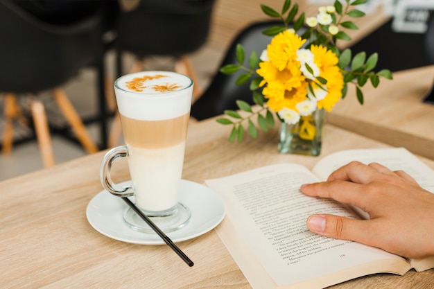 Person reading book near coffee cup on desk at caf�