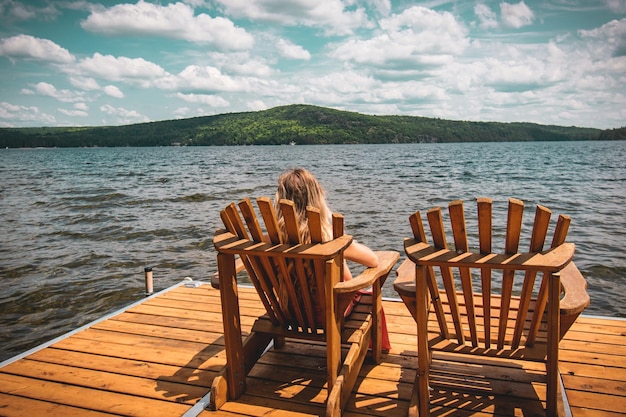 Person resting on a folding chair on a wooden dock on the sea under a cloudy sky and sunlight